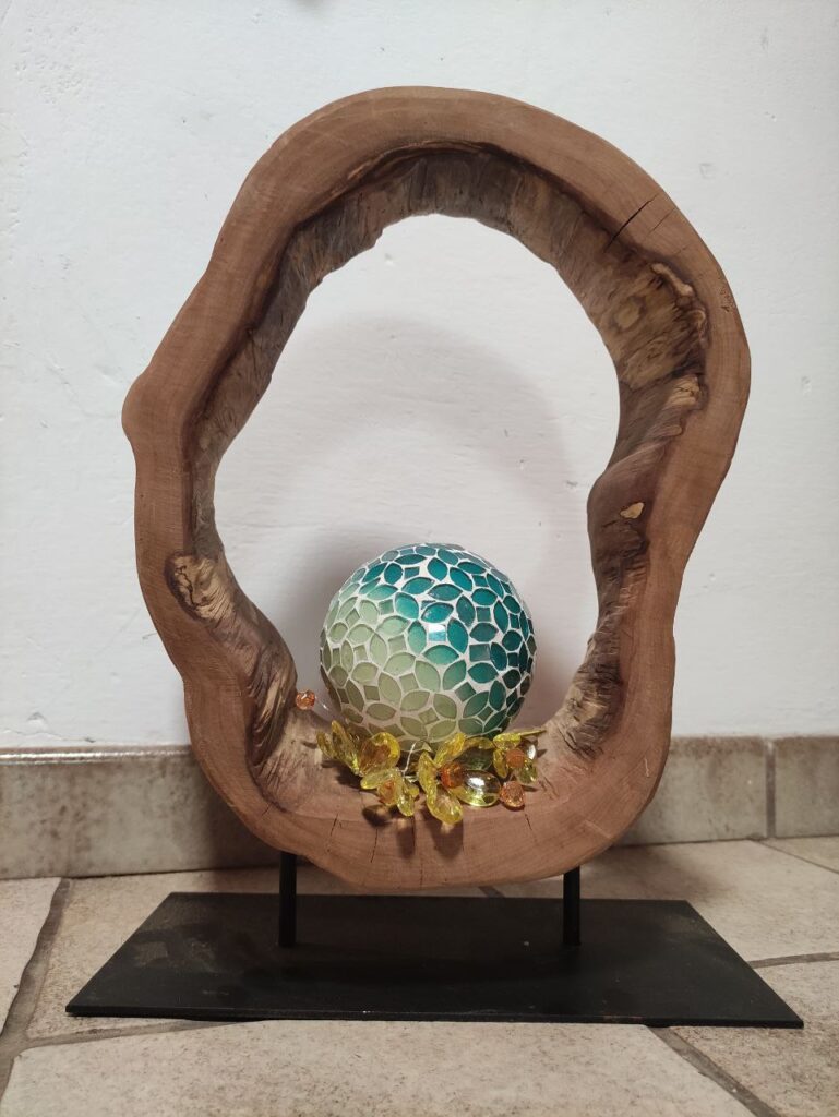 Ausgehöhlte Baumscheibe auf Metallständer mit Dekokugel und Blüten in der Mitte