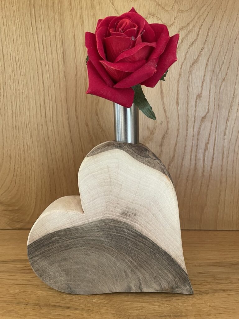 Holzherz mit oben eingefrästem Loch in dem eine Metallvase mit Rose steckt