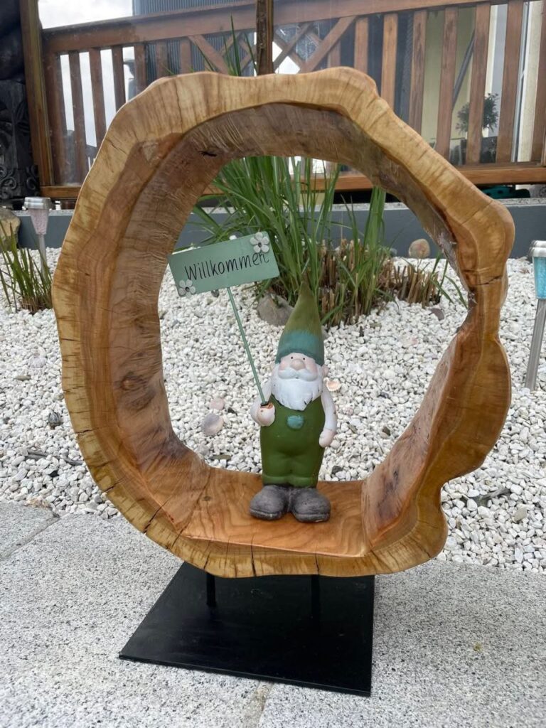 Ausgehöhlte Baumscheibe auf Metallständer mit Gartenzwerg und Schild mit Aufschrift, Willkommen